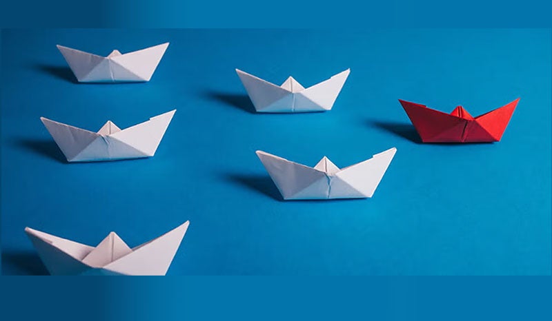 A red paper boat leading white boats, symbolizing leadership and innovation.